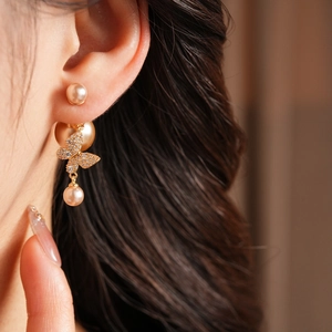 Close-up of butterfly pearl earrings with gold plating and cubic zirconia on a model