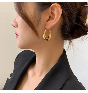 Close-up of golden polished waterdrop hoop earrings worn by a model in a modern style