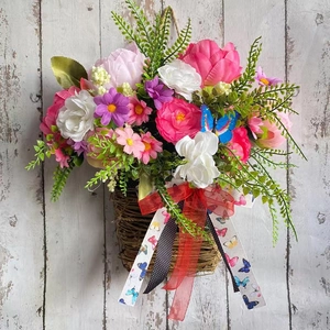 Close-up of pink peonies and daisies in a rattan basket with a red organza bow