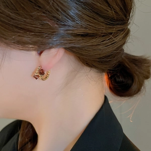 Detail of twisted gold earrings with square brown gemstones worn by a model