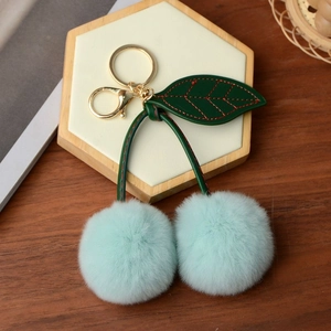 Detail of mint green faux rabbit fur cherry keychain with green leather leaf on stand