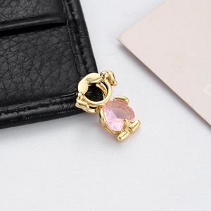 Close-up of a gold-plated heart pendant with a pink teardrop gemstone on a leather surface