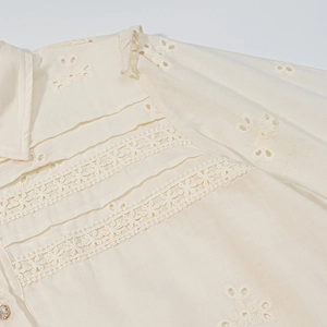 Detail of off-white blouse with eyelet embroidery, lace trim, and a pearl button