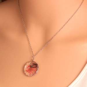 Detailed close-up of a glass pendant necklace with dried flowers and butterfly charms