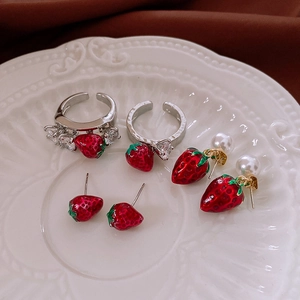 Detailed macro view of red enamel strawberry jewelry set with pearls on white porcelain