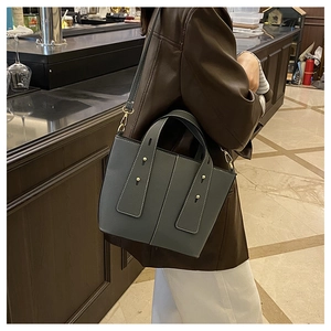 Détail du sac seau en cuir bleu-gris avec texture litchi et rivets dorés élégants