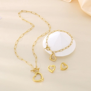 Detailed set of gold titanium necklace, bracelet and heart earrings on beige fabric