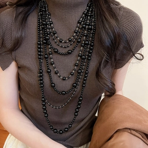 Close-up of a layered black acrylic beaded long necklace on a brown sweater background