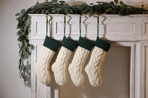 Close-up of four cream knitted Christmas stockings with green cuffs hanging on a fireplace