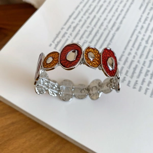 Detailed view of irregular silver bracelet with red and orange enamel on an open book