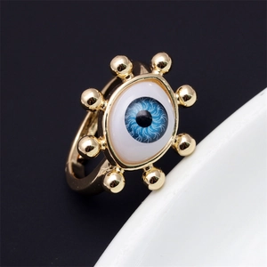 Close-up of gold-plated geometric evil eye ring with blue enamel on white ceramic