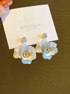 Detailed macro view of white enamel camellia flower earrings with sparkling zircon centers