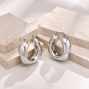 Detailed close-up of polished silver hollow hoop earrings on a stone texture display