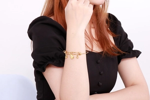Close-up of a gold-plated stretch bracelet featuring a guitar charm on a model's wrist