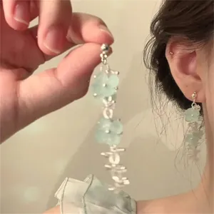 Detail of light blue acrylic flower tassel earrings worn with an elegant silver needle drop