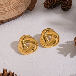 Close-up of golden twisted triangle earrings on a wooden base with decorative pine cones