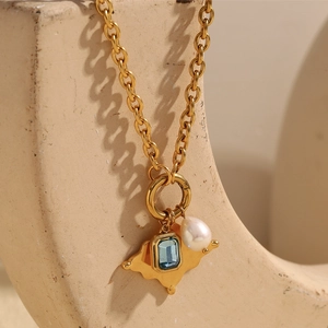 Detail of 18K gold-plated necklace with blue gemstone and pearl on textured background