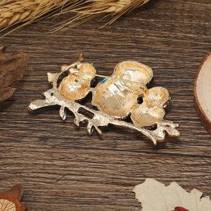 Golden owl brooch back view showing the pin fastener on rustic dark wood background