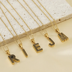 Détail de pendentifs lettres dorées avec rayures noires sur de fines chaînes à maillons