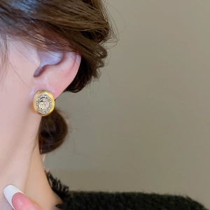 Close-up of gold oval stud earring with central gemstone and pavé diamonds on ear