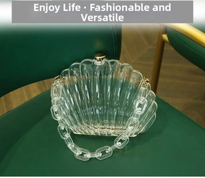 Detail der transparenten Acryl-Clutch in Muschelform mit Goldverschluss auf grünem Stuhl