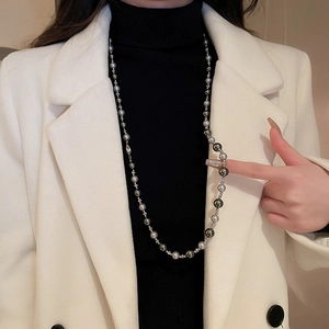 Détail du collier de perles gris et argent sur un pull à col roulé noir élégant