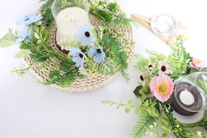 Close-up of pink and blue daisy flower wreath with a white scented candle in a glass holder