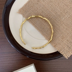 Close-up of golden hammered cuff bangle with irregular wave texture on rustic background