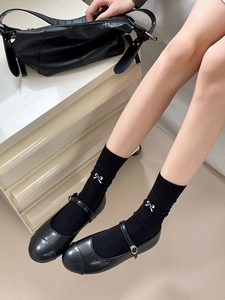Detail of black mid-calf socks with white bow embroidery worn with Mary Jane shoes