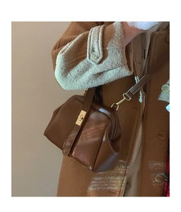 Close-up of retro dark brown leather handbag with gold metal clasp and pleated texture