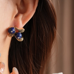 Close-up of vintage gold flower earring with blue beads and diamonds on model ear