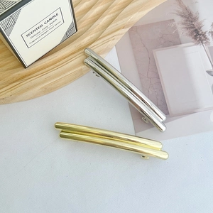 Fermagli geometrici minimalisti in oro e argento presentati su un vassoio di legno