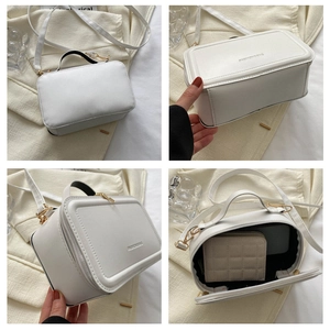 Detail view of white square handbag with golden hardware and spacious interior compartment