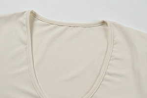 Detail shot of the deep V-neckline showing neat stitching on cream pleated dress