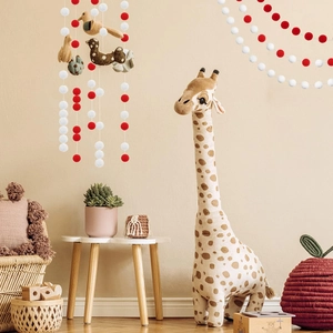 Red and white felt ball garland with a cute bird and plush giraffe in a cozy nursery