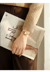 Elegant gold square watch with metal chain strap on female wrist with magazine