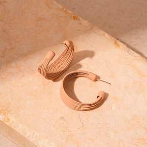 Macro shot of khaki C-shaped layered earrings featuring a brushed minimalist texture