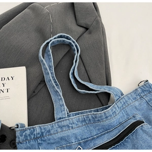 Detail of blue denim tote bag showing reinforced strap stitching and black front zipper pocket