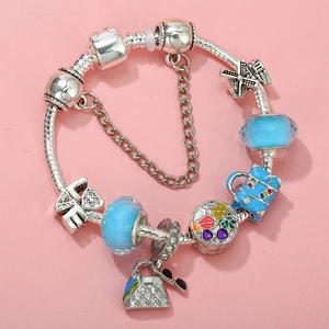 Detail of silver snake chain bracelet with blue crystals and travel-themed charms on pink background