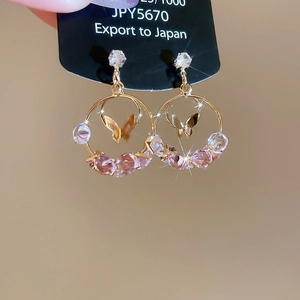 Close-up of golden hoop earrings featuring a butterfly pendant and sparkling pink crystals