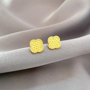 Gold lucky clover stud earrings with dotted texture on gray silk fabric background