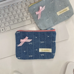 Dettaglio del portamonete in denim con fiocco rosa e ricamo vicino a un laptop bianco