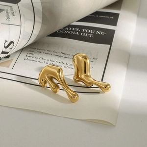 Detailed close-up of golden fluid-shaped lava earrings on minimalist newspaper background