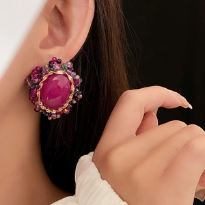 Close-up of vintage magenta oval earring with colorful beadwork and gold wire detail
