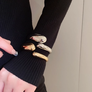 Close-up of minimalist water drop open bangle in polished gold and silver metallic finish