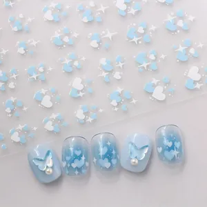 Detail of blue heart nail stickers with 3D butterfly and pearl accents on gradient nails