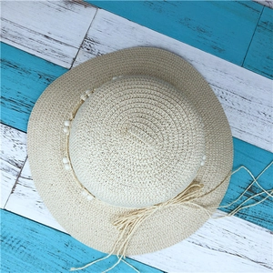 Top view of beige straw sun hat with beaded trim and bow on vintage wood background