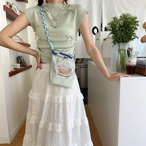 Detail of green crossbody bag with carousel embroidery and white lace cake skirt