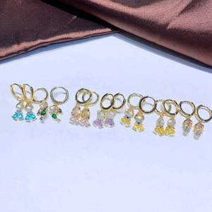 Goldene Ohrringe mit bunten Zirkonia-Anhängern und Perlen auf Seidenhintergrund