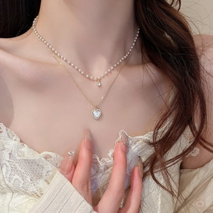 Detail of double-layer gold necklace featuring a heart pendant and white pearls on model